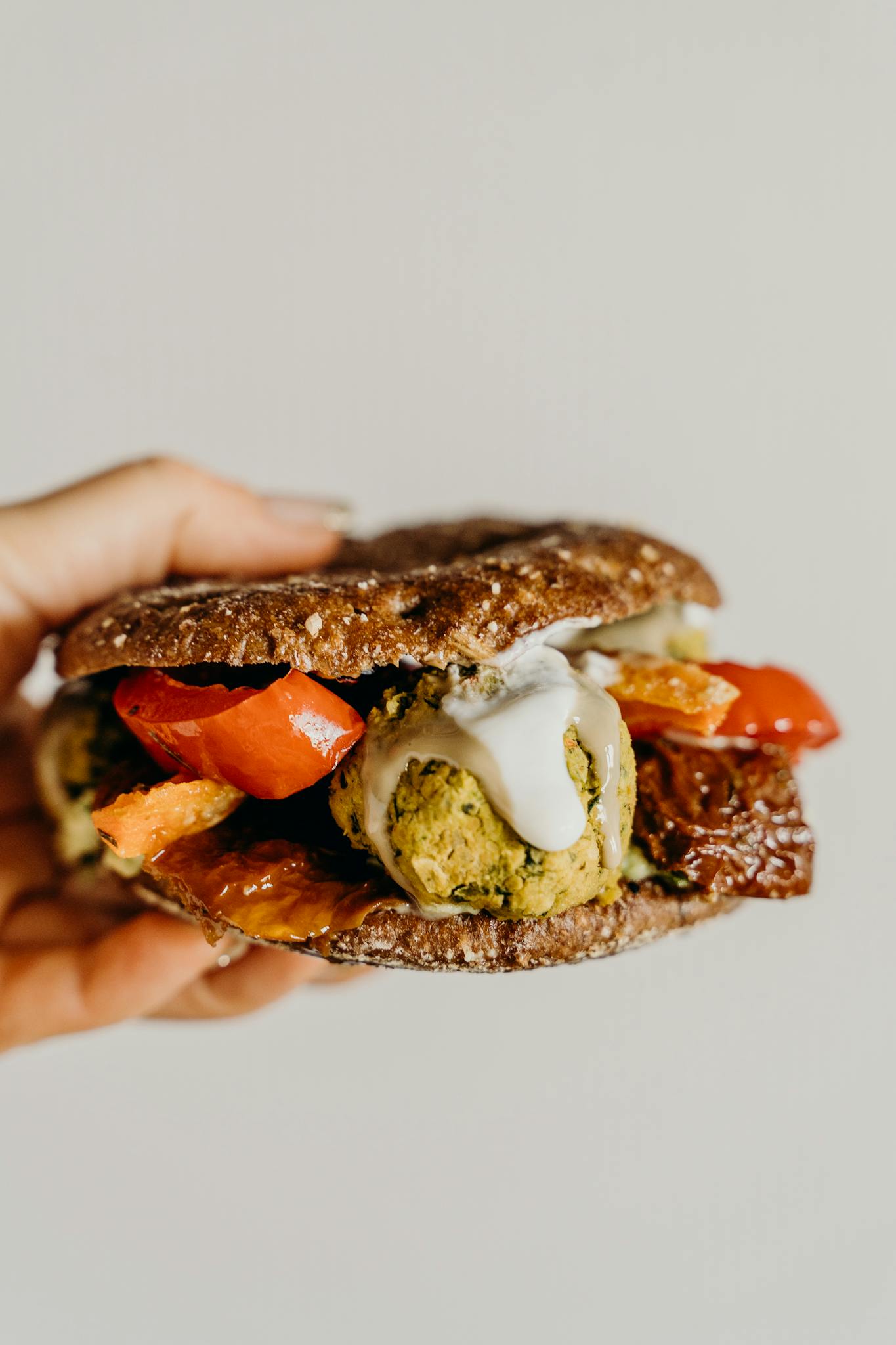 Hand holding a delicious falafel sandwich with vibrant vegetables and creamy sauce.